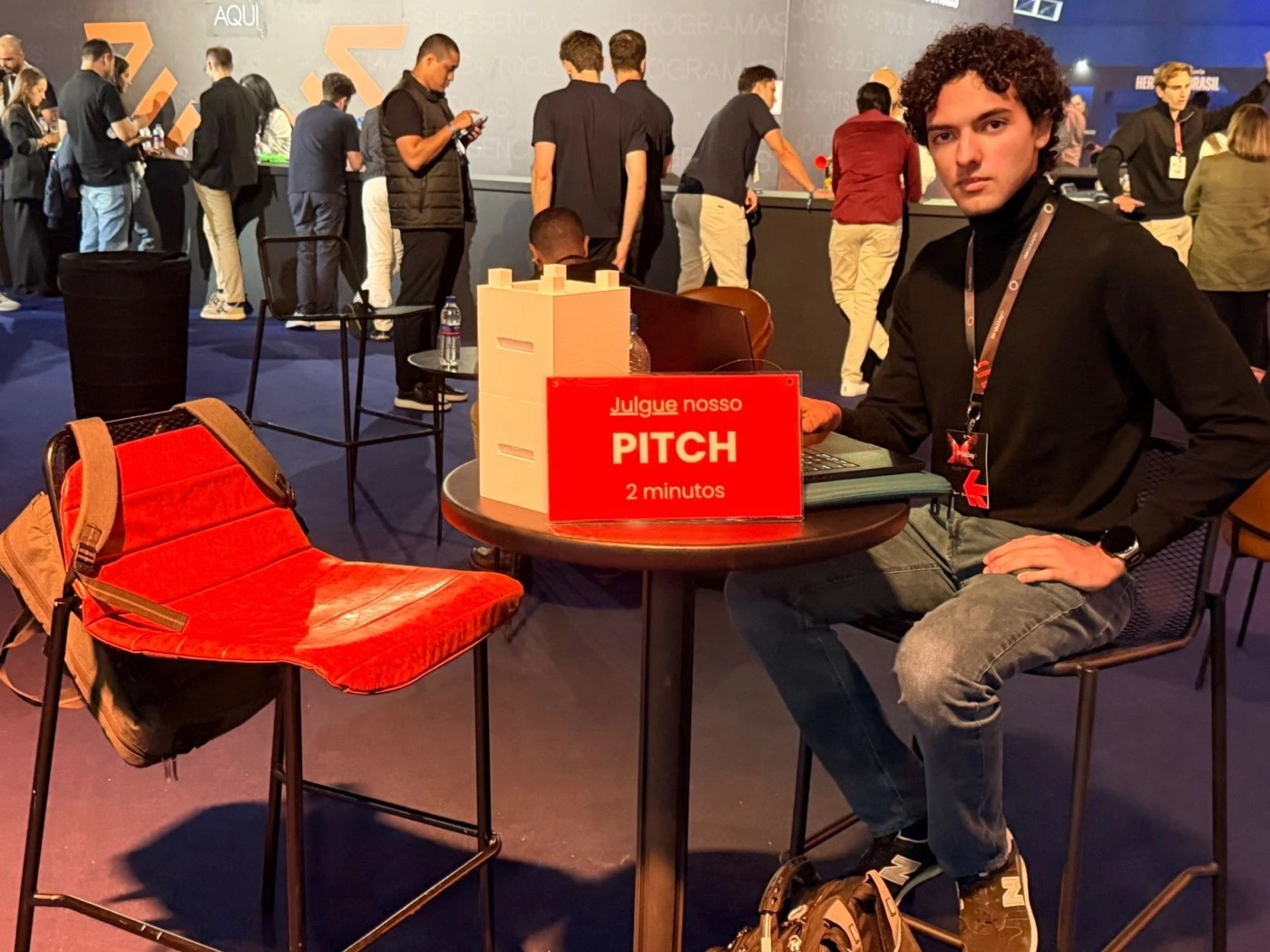Antony na mesa de pitch com o protótipo do Bloco Bind e a placa: julgue nosso pitch, 2 minutos